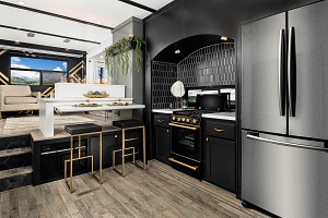 Photo of the kitchen in a Keystone Montana concept fifth wheel. There is a chrome French door refrigerator next to counters with black cabinetry and a black range/oven. Two stools sit next to a breakfast bar.