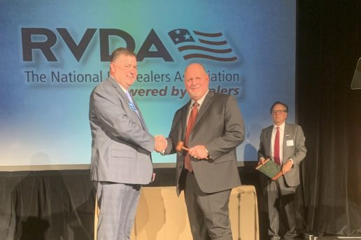 Outgoing RVDA Chairman Mike Regan passes the gavel to new Chairman Ron Shepherd, while RVDA President approaches to award a plaque to Regan.