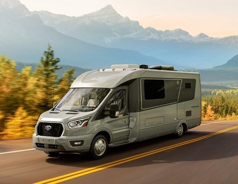 A picture of a gray Type C RV on a two-lane highway with mountains and trees in the background.