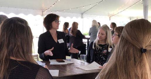 RV Women's Alliance president Susan Carpenter speaks to other women at a table inside of a white tent