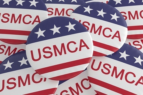 A picture of a pile of campaign buttons that say, "USMCA" on them. The buttons have a strip of blue with white stars on top and red and white stripes on the bottom.