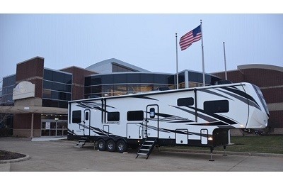 A picture of a Jacyco fifth wheel toy hauler in front of a building and an American flag