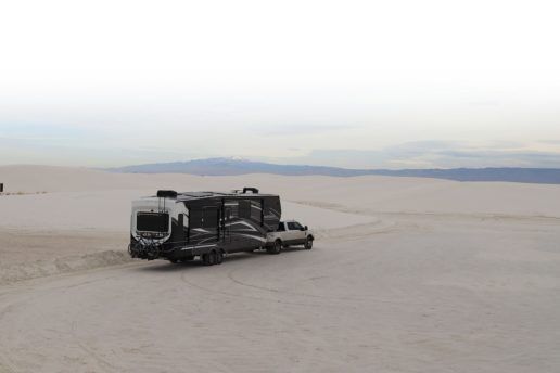 A truck pulls a Keystone RV 2020 Montana Super SolarFlex through a white, sandy desert with mountains in the distant background