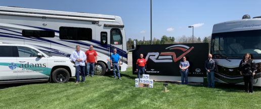A photo of seven REV Group associates standing on grass in front of two RVs and an Adams County Emergency Medical Service truck with medicals masks they are donating to the Adams Memorial hospital.