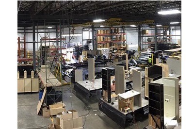A picture of the inside of a manufacturing plant. There are shelves and boxes and scraps of wood around various work stations.